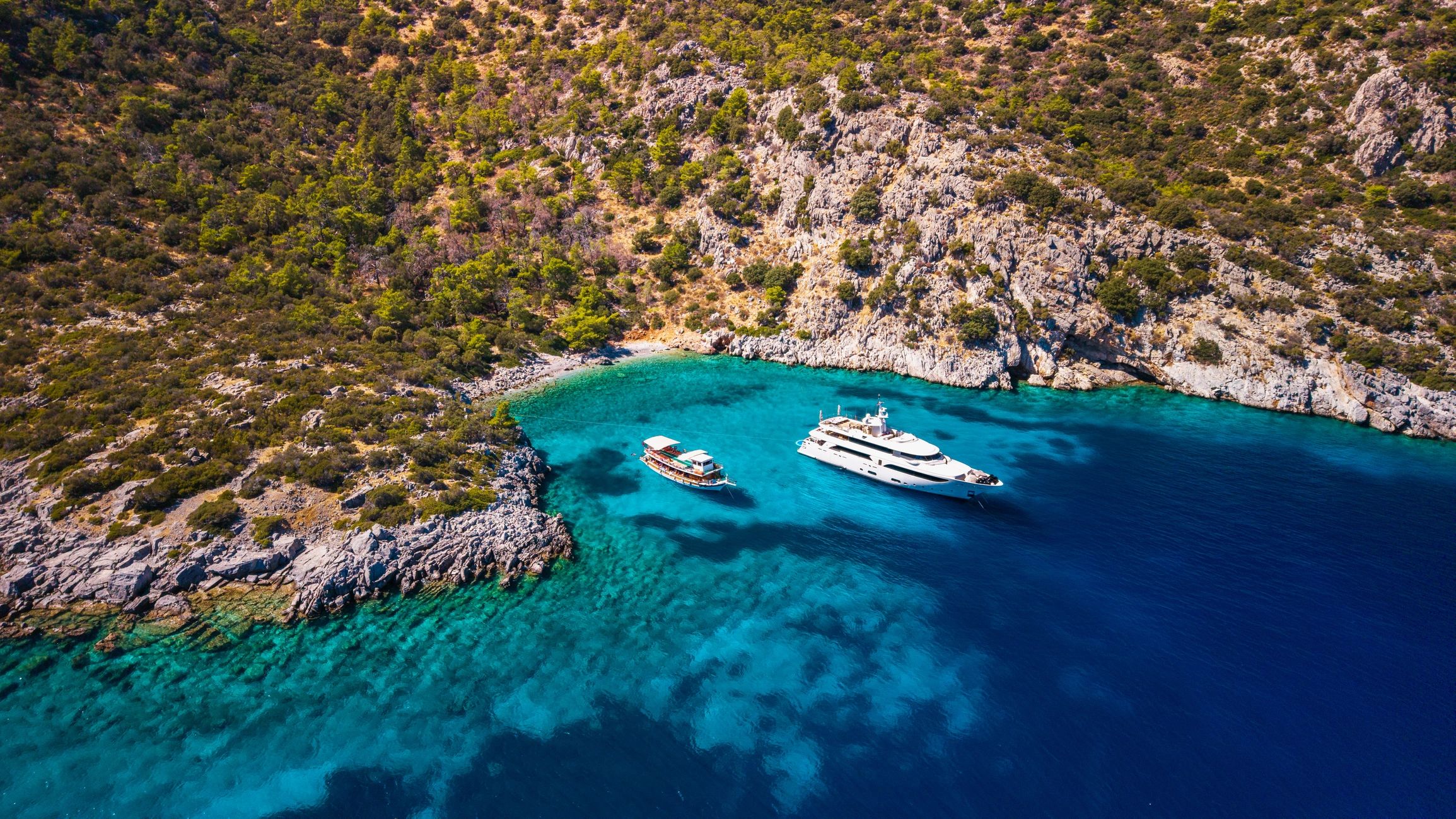 Tour boat and luxury yacht anchored in a bay in the Aegean Sea, aerial view